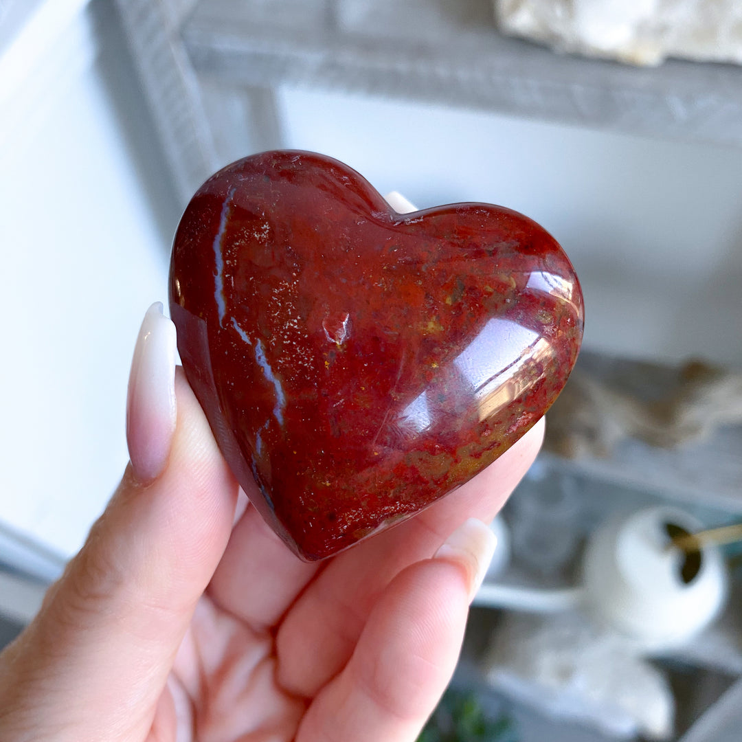 Heart-shaped red stone held in a hand with a blurred background