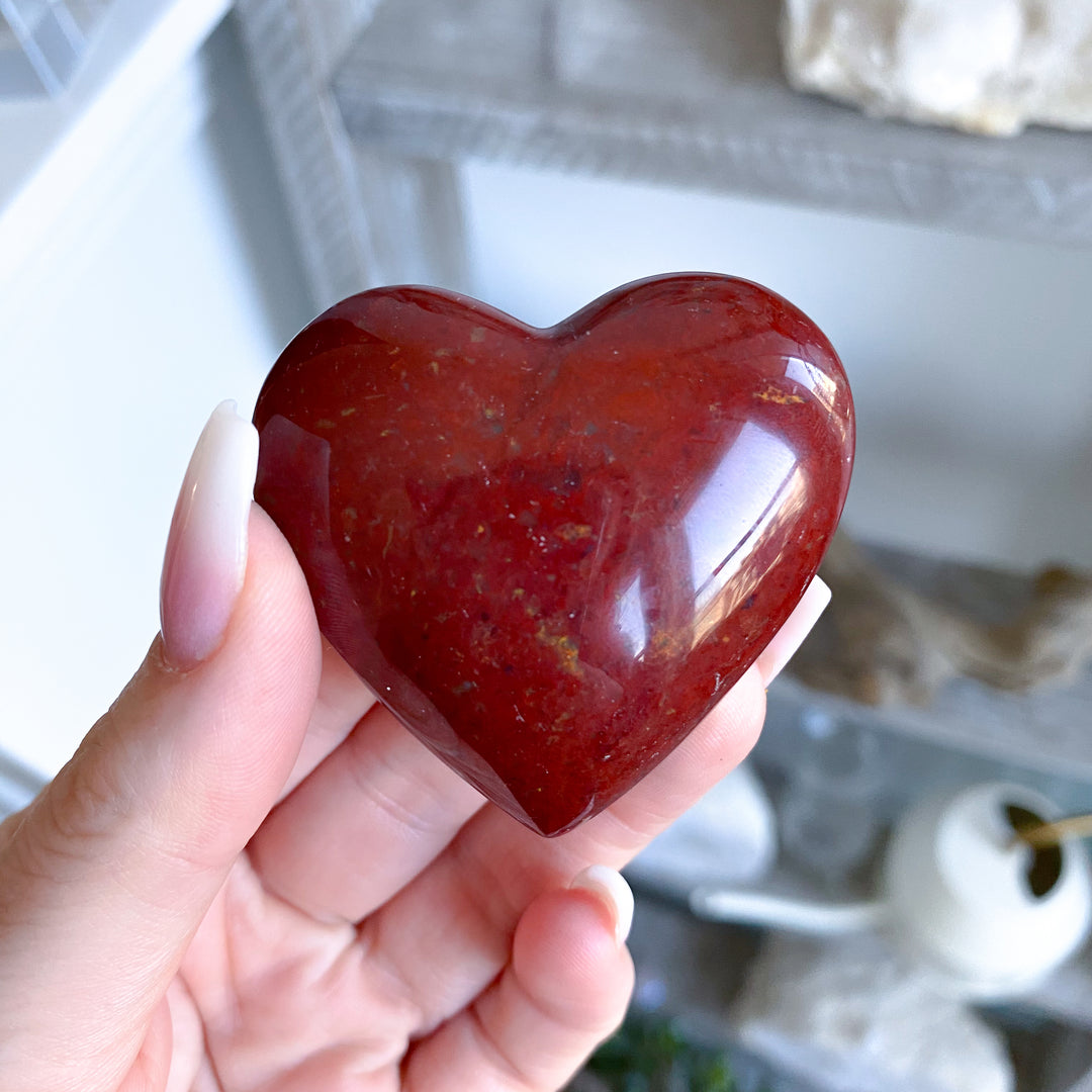 Heart-shaped red stone held in a hand with a blurred background