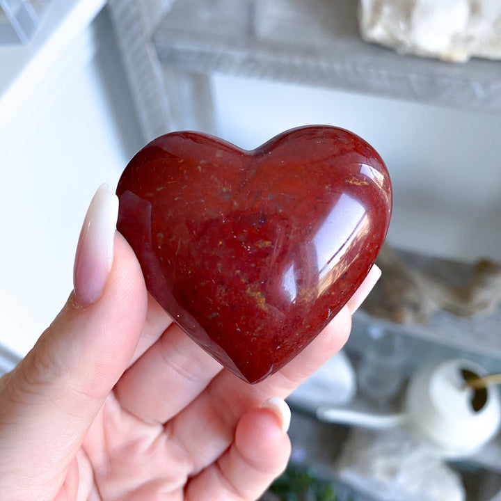 Heart-shaped red stone held in a hand with a blurred background