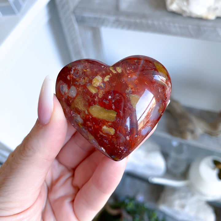 Heart-shaped red stone held in a hand with a blurred background