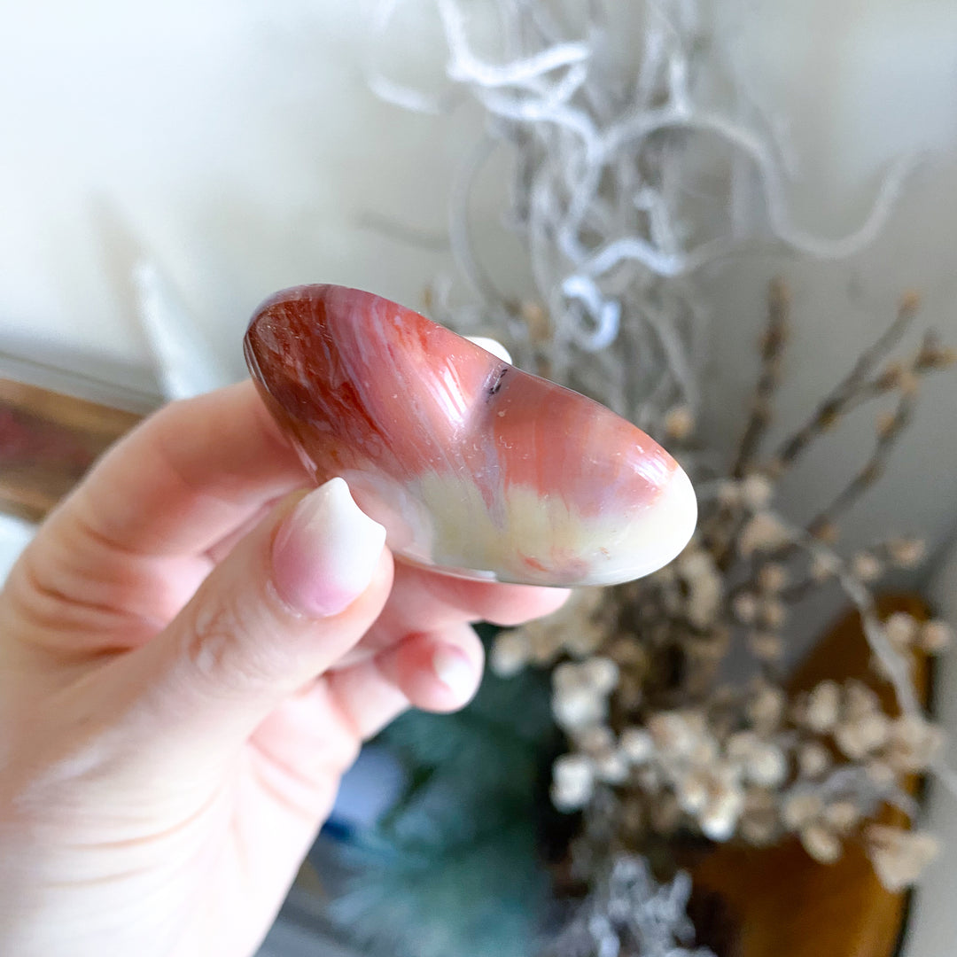 Hand holding a red and white stone with a blurred indoor background