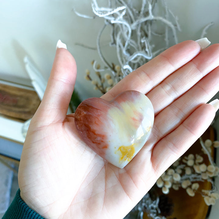 Heart-shaped stone held in a hand with a blurred indoor background