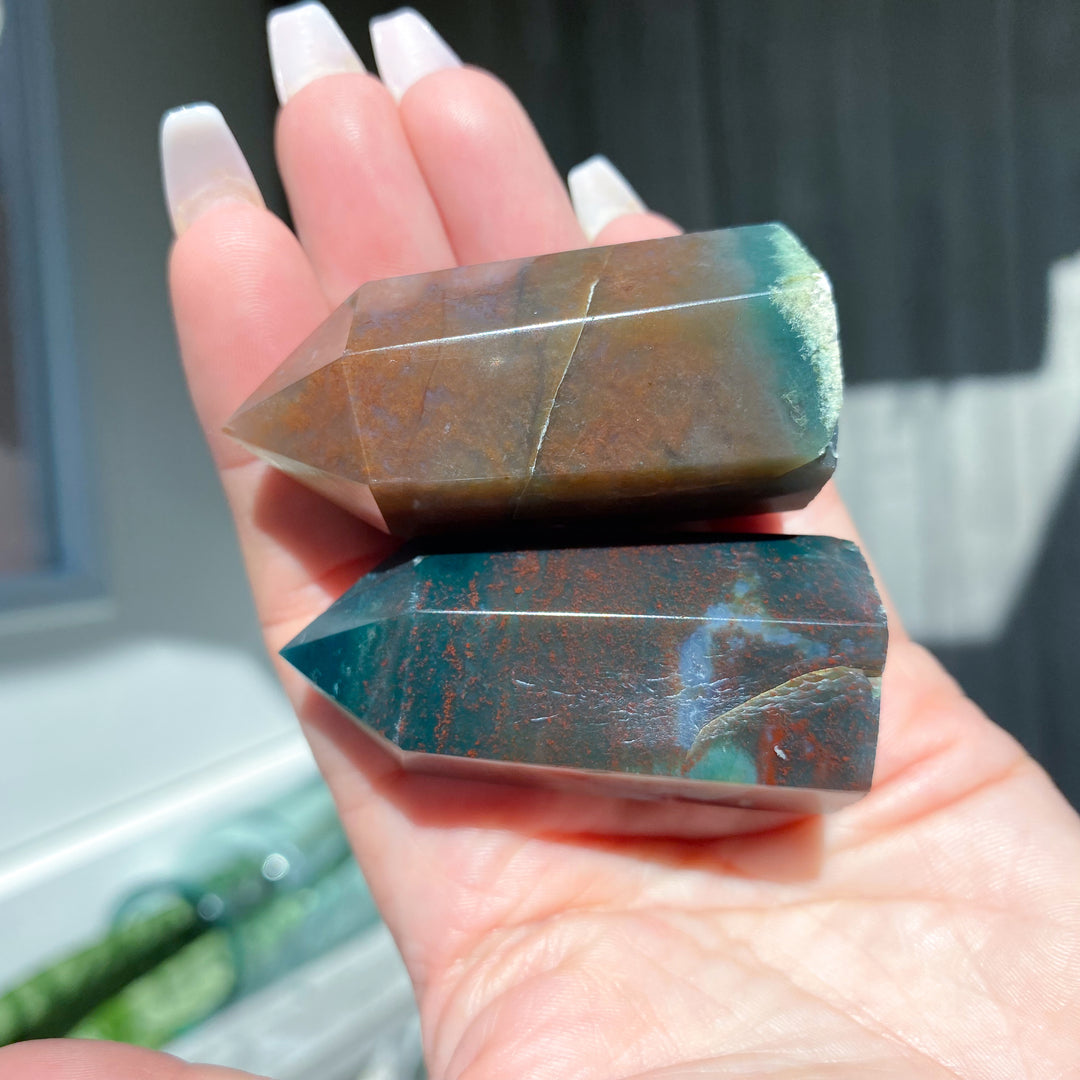 Hand holding two green and brown crystal points with a blurred background