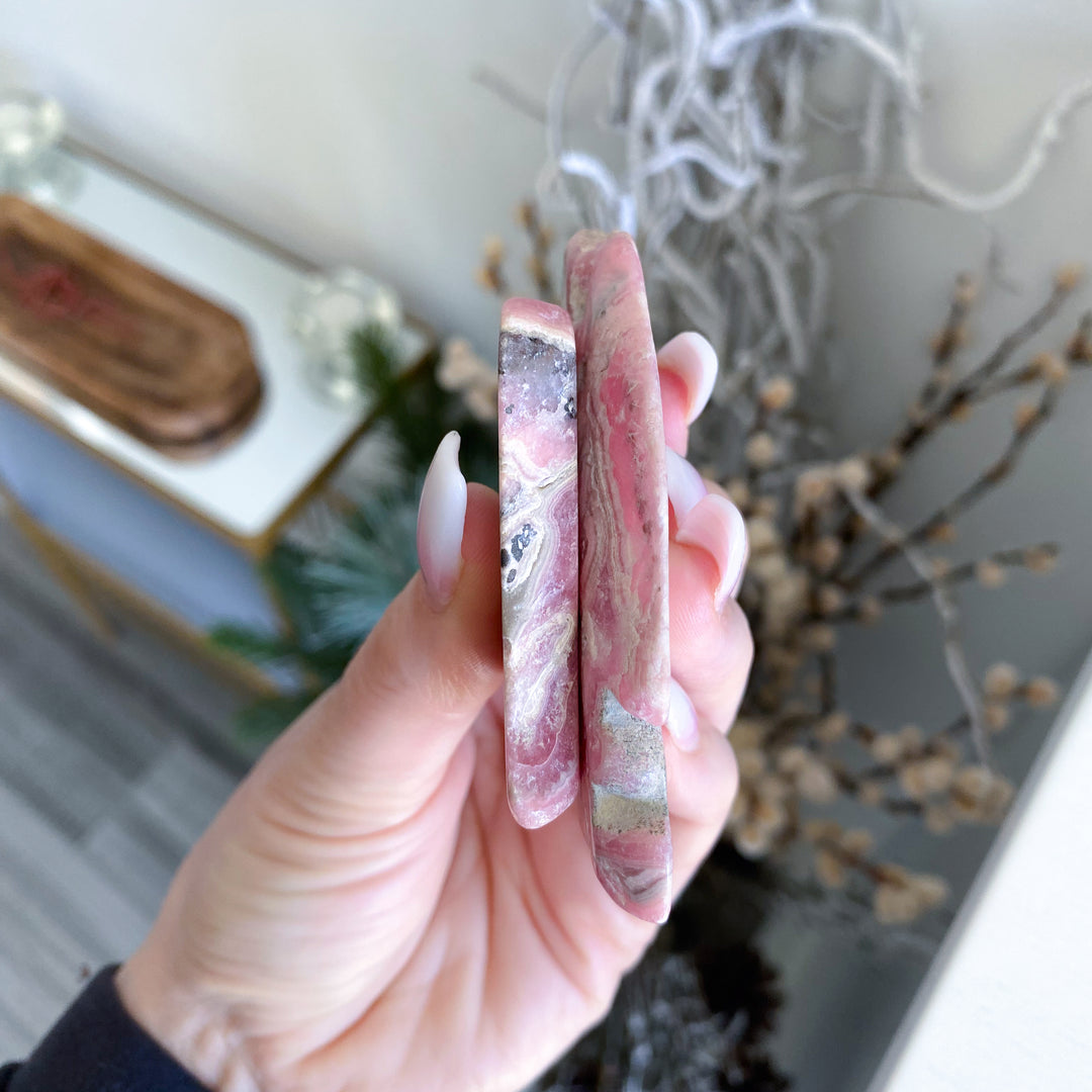 Hand holding two marbled pink and gray stones with a blurred indoor background
