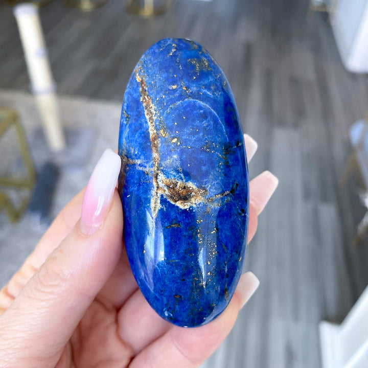 Hand holding a blue stone with gold veins against a blurred indoor background