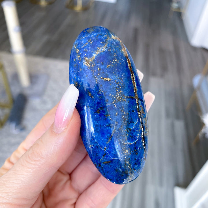 Hand holding a blue stone with gold veins against a blurred indoor background