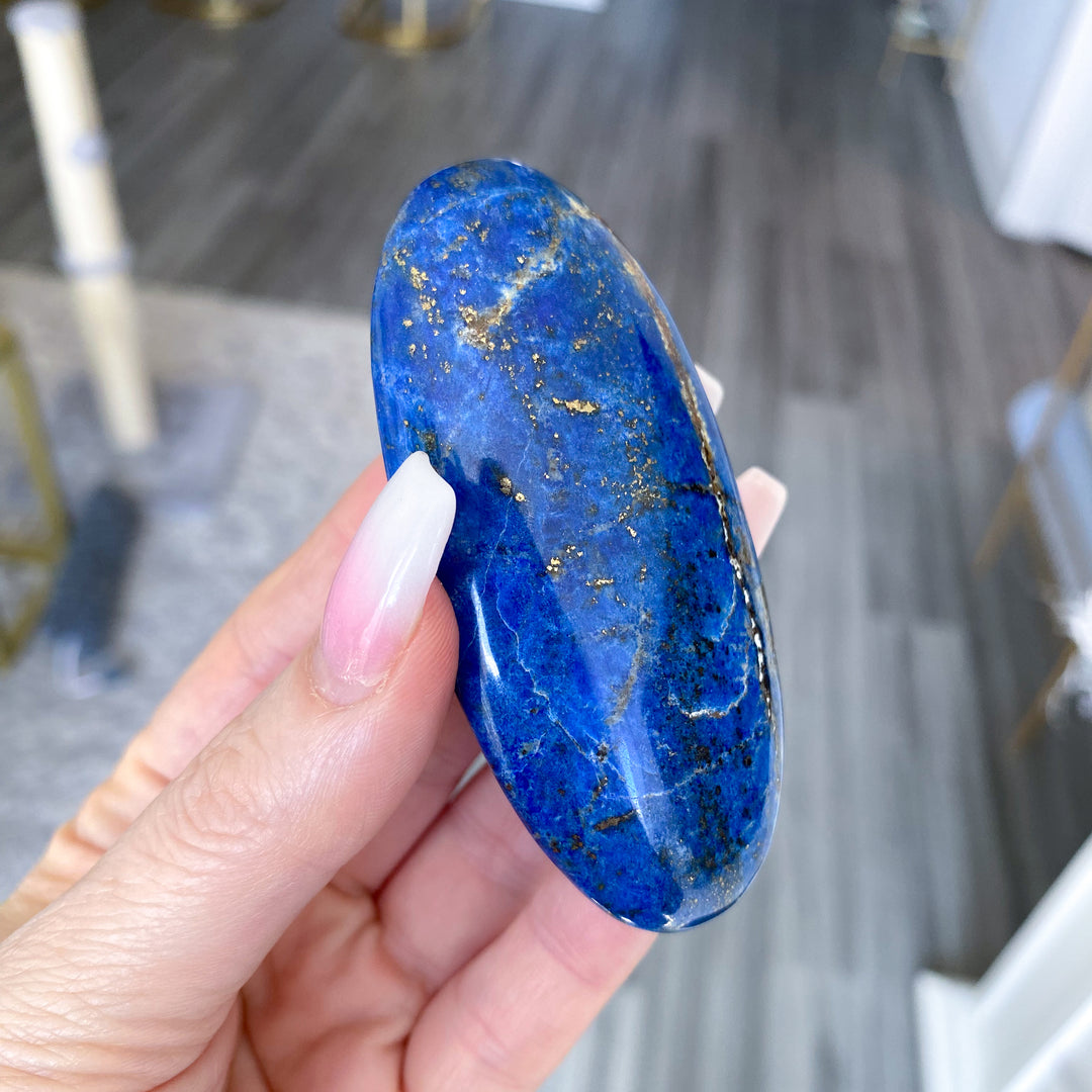 Hand holding a blue stone with gold specks against a blurred indoor background