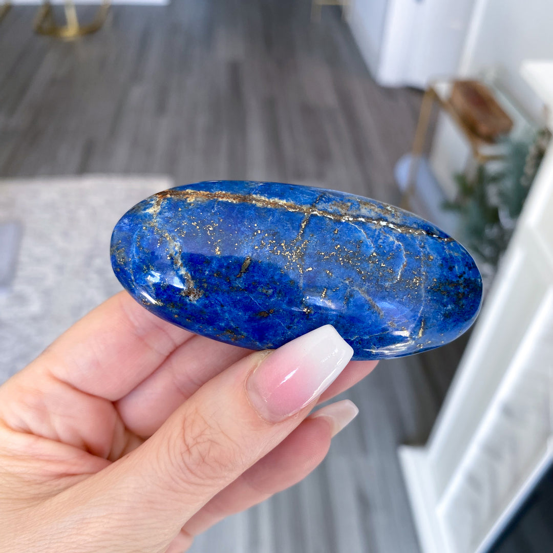 Hand holding a blue stone with gold veins indoors