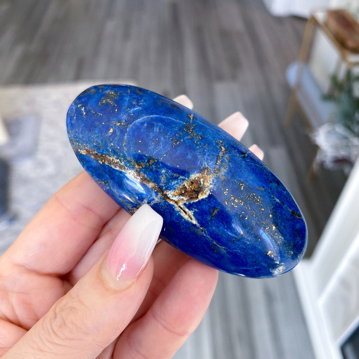 Hand holding a blue stone with gold specks on a blurred indoor background