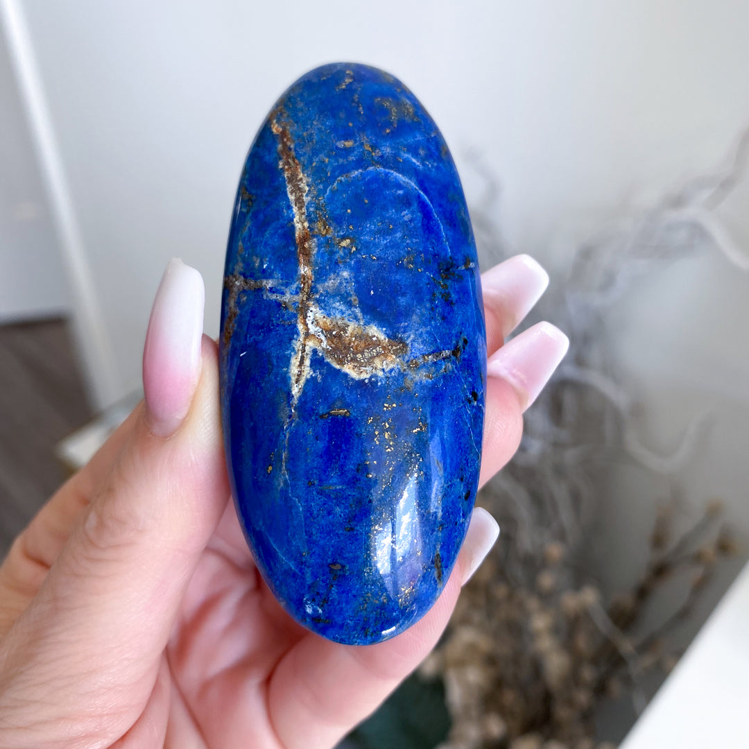 Hand holding a blue stone with gold veins against a blurred indoor background