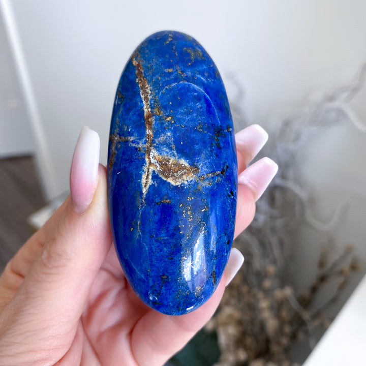 Hand holding a blue stone with gold veins against a blurred indoor background