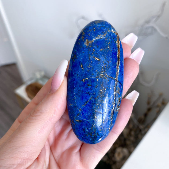 Hand holding a blue stone with gold specks against a blurred indoor background