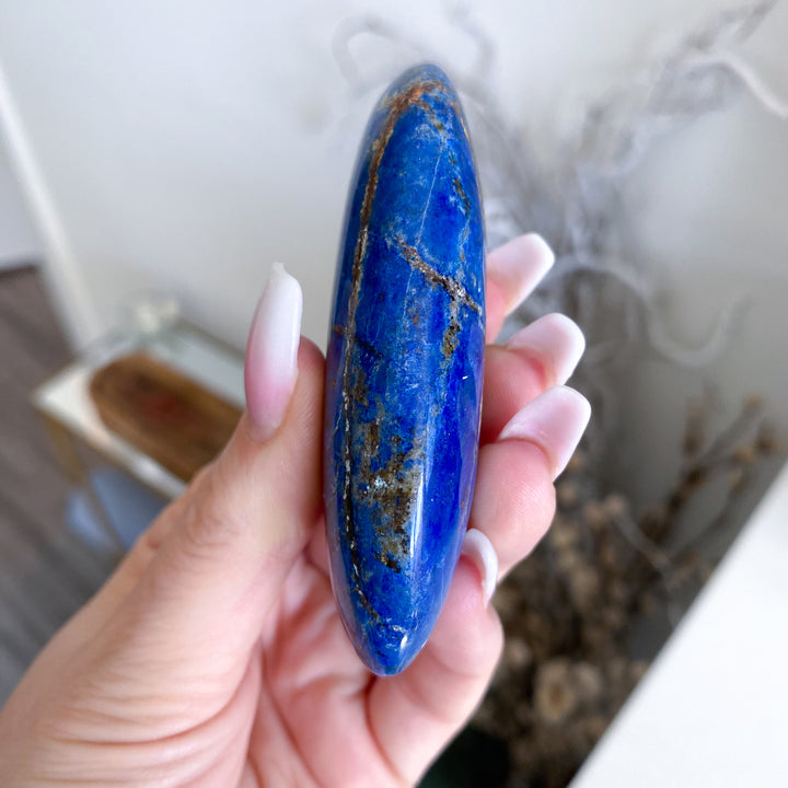 Hand holding a blue stone with gold veins against a blurred indoor background