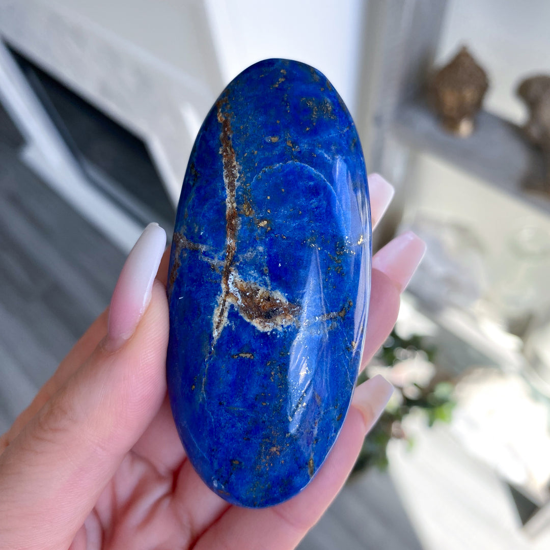 Blue stone with gold veins held in a hand against a blurred indoor background