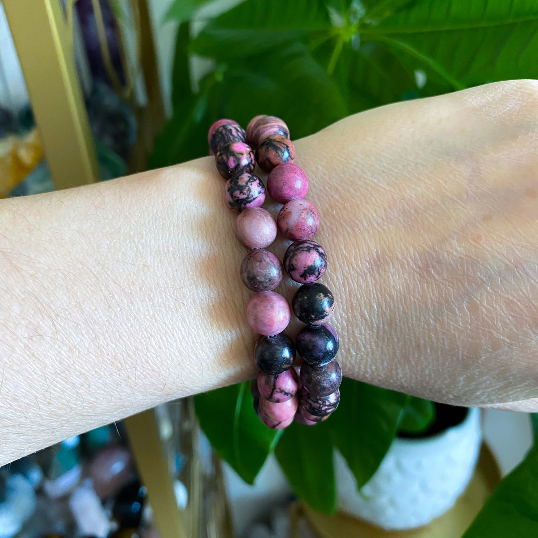 Two beaded bracelets on a wrist with a blurred green plant background
