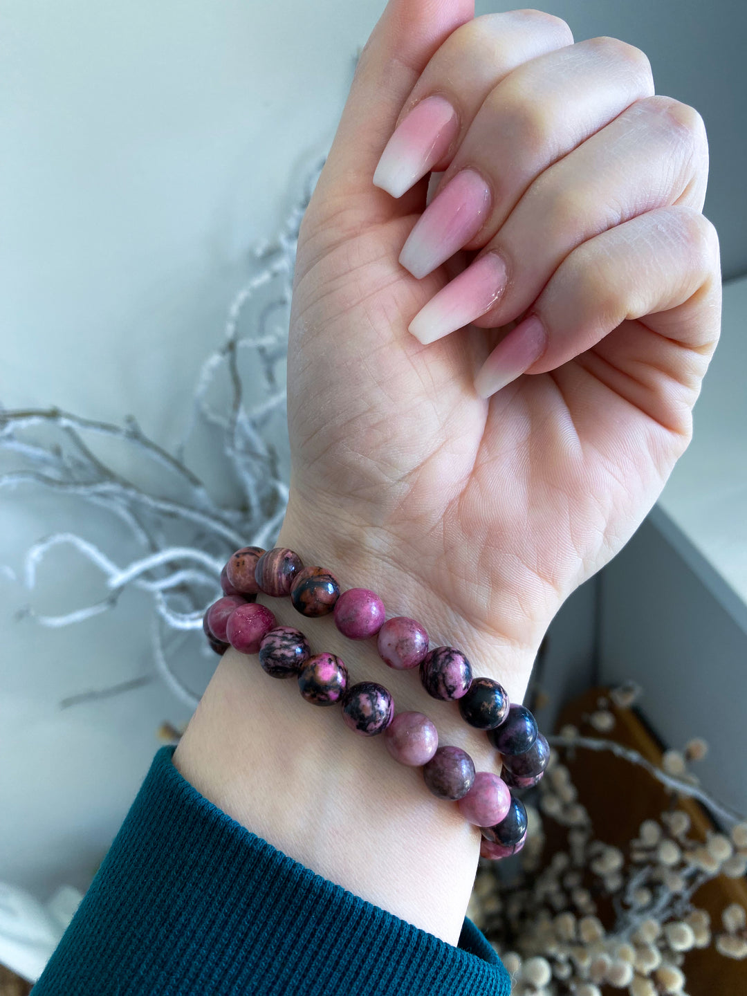 Hand wearing a bracelet with pink and purple beads against a neutral background