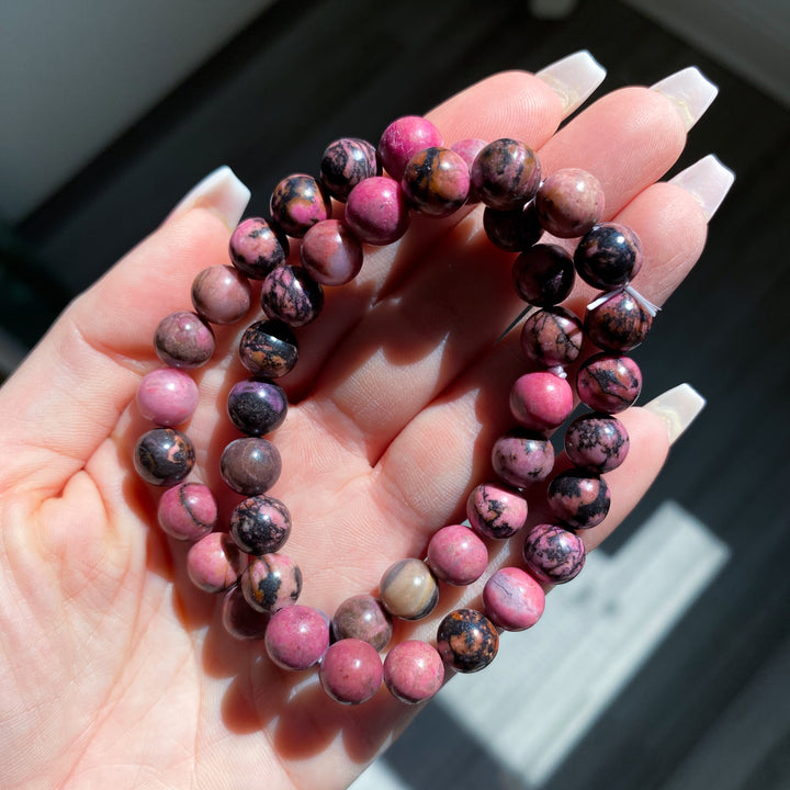 Hand holding a stack of pink and black beaded bracelets.