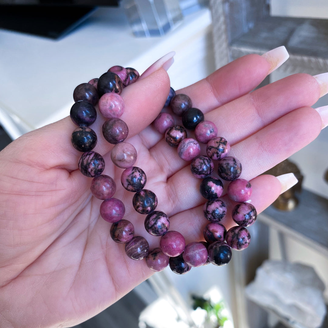 Hand holding two beaded bracelets with a blurred indoor background
