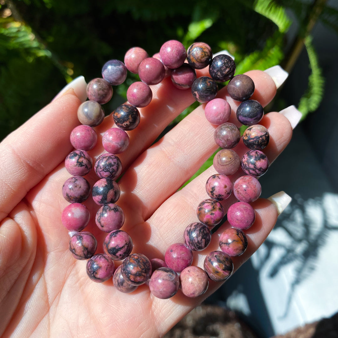 Hand holding two pink and purple beaded bracelets with a natural background